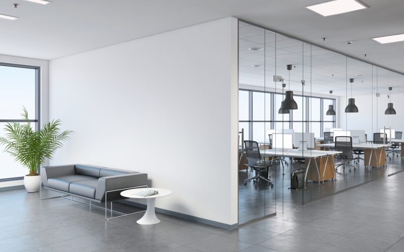 Modern business office space with lobby Interior view of a modern office, business template. Left side of the picture is large sofa with a plant and coffee table. Blank wall for copy space. On the right, many office desks with pendant lights above. large windows. gray floor tiles, white walls. Render